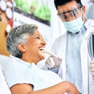 Woman smiling at reflection in handheld mirror with dentist