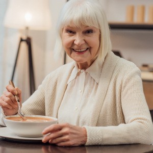 A smiling senior woman eating soup at home