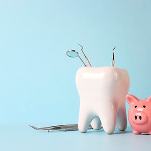 A large model tooth next to a pink piggy bank and dental tools