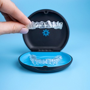 An Invisalign tray behind held above its carrier case with a light blue background