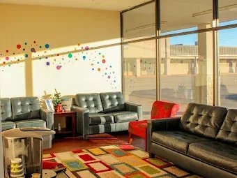 Waiting room at Sonria Dentista Commerce with leather sofas, a colorful rug and large windows