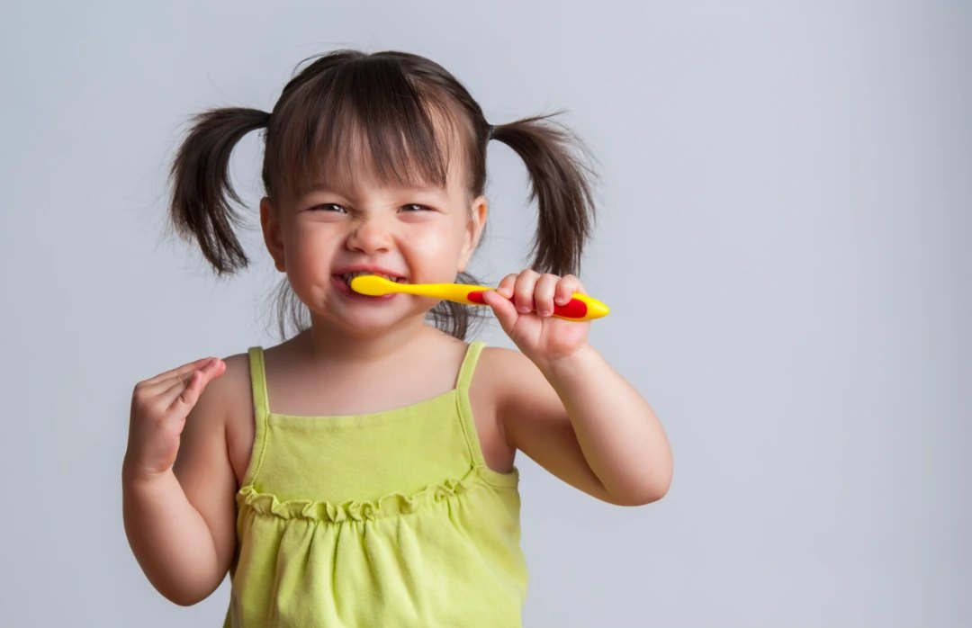 Toddler brushing teeth with a yellow toothbrush
