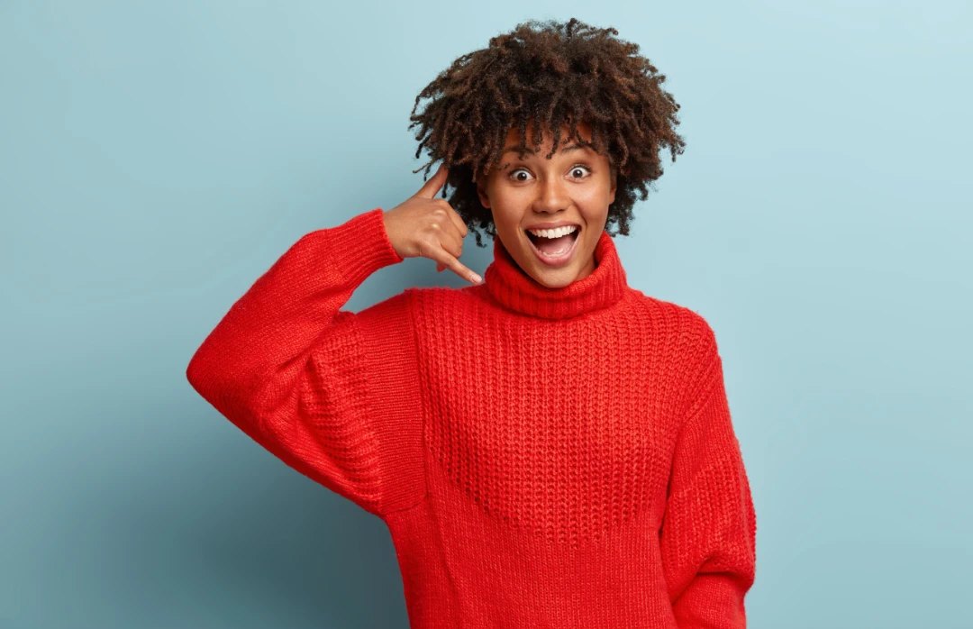 Smiling woman making a phone gesture to call and book a visit